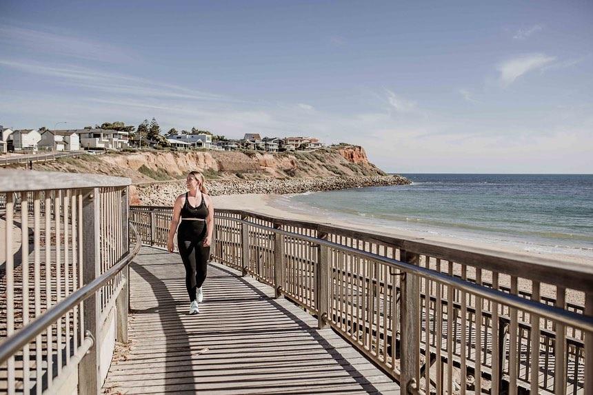 Owner of BeYou Activewear walking along the boardwalk at the beach wearing the black maternity activewear support leggings and black breastfeeding friendly crop top. 